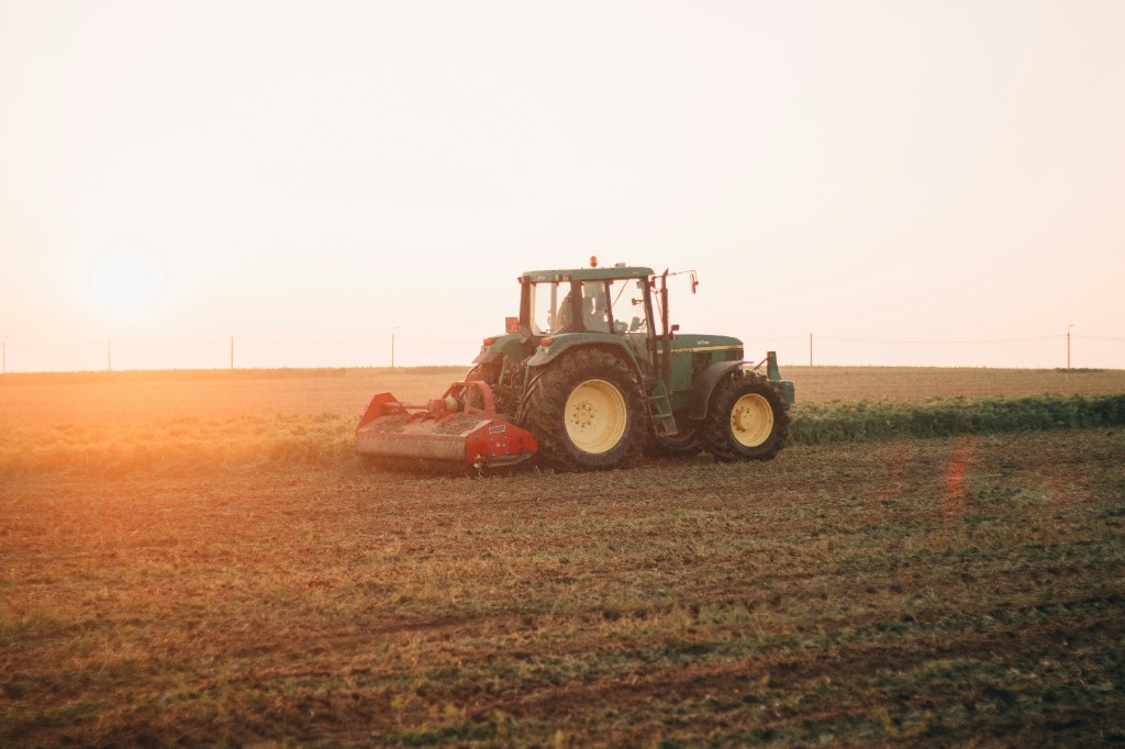 John Deere tractor op landbouwgrond bij zonsondergang